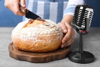 Woman making ASMR sounds with microphone and bread at grey table, closeup