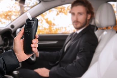 Image of Police officer with breathalyzer and man in car. Alcohol consumption while driving