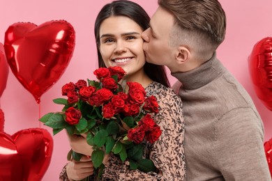 Photo of Happy couple celebrating Valentine's day, beloved woman with bouquet of red roses on pink background