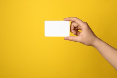 Photo of Woman holding blank gift card on yellow background, closeup