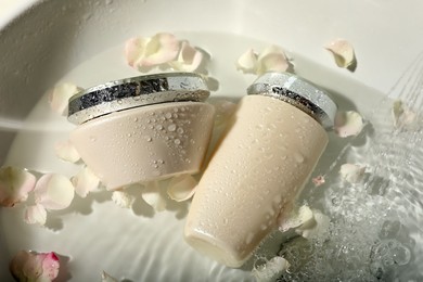 Hair care cosmetic products with flower petals and water in sink, above view