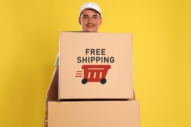 Happy young courier with cardboard boxes on yellow background. Free shipping
