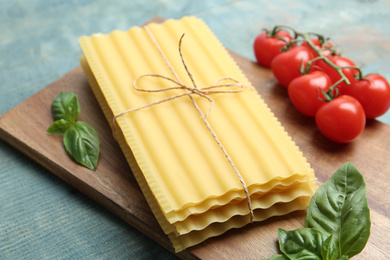 Uncooked lasagna sheets with basil and cherry tomatoes on blue wooden table, closeup