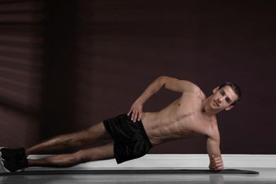 Handsome man doing side plank exercise on floor indoors