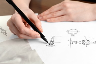 Photo of Jeweler drawing sketch of elegant ring on paper at table, closeup