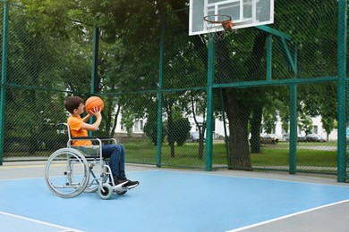 Disabled teenage boy in wheelchair playing basketball  on outdoor court