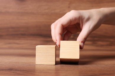 Photo of Woman arranging cubes on wooden background, closeup. Idea concept
