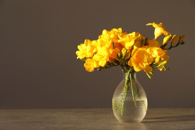 Beautiful yellow freesia flowers in glass vase on grey table, space for text