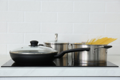 Pot with uncooked pasta and frying pan on stove in kitchen