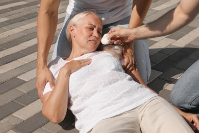 Men helping mature woman outdoors. Suffering from heat stroke