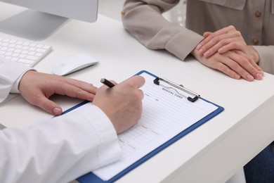 Doctor filling out patient's medical card at table in clinic, closeup