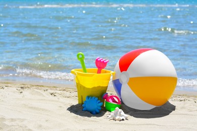 Photo of Set of plastic beach toys and inflatable ball on sand near sea. Space for text