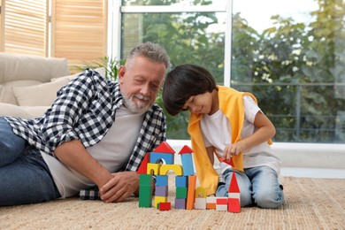 Happy grandfather and his grandson playing with toy building blocks together at home