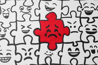Drawing of white puzzle pieces and one red with different emotions, closeup. Bullying concept