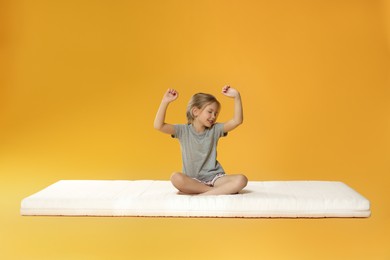 Photo of Little girl waking up on mattress against orange background