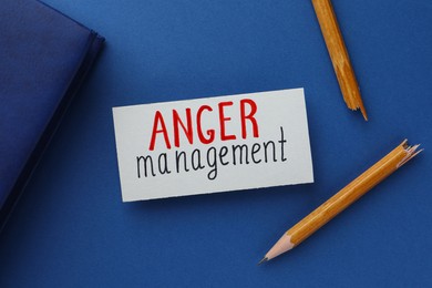 Card with words Anger Management, notebook and broken pencil on blue background, flat lay