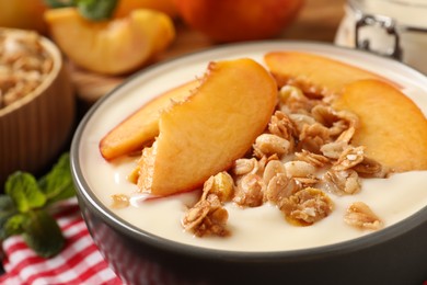 Tasty peach yogurt with granola and pieces of fruits in bowl on table, closeup