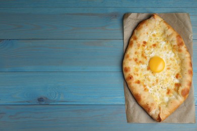 Fresh homemade khachapuri with cheese and egg on light blue wooden table, top view. Space for text