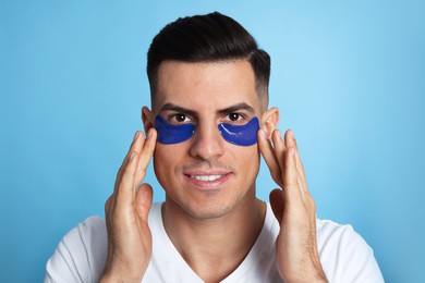 Man applying under eye patches on light blue background