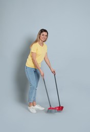 Photo of Young woman with broom and dustpan on grey background