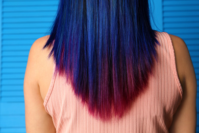Young woman with bright dyed hair on blue wooden background, back view. Closeup