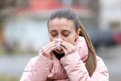 Ill woman with paper tissue sneezing outdoors