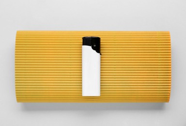 Photo of Stylish small pocket lighter with yellow corrugated fiberboard on white background, top view
