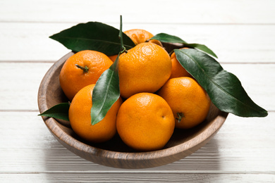 Fresh ripe tangerines with leaves in bowl on white wooden table. Citrus fruit