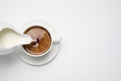 Pouring milk into cup of coffee on white background, top view