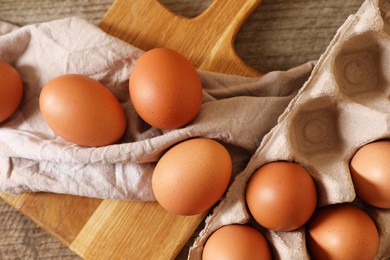 Photo of Raw chicken eggs with carton, napkin and board on wooden table, flat lay
