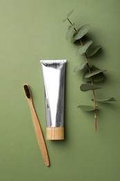 Bamboo toothbrush and tube of paste on green background, flat lay. Conscious consumption