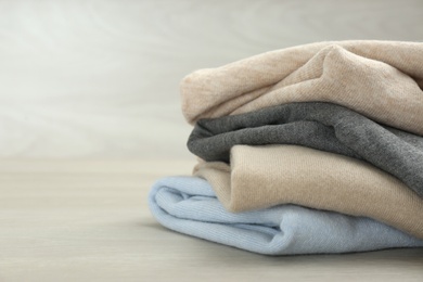 Photo of Stack of cashmere clothes on wooden table. Space for text