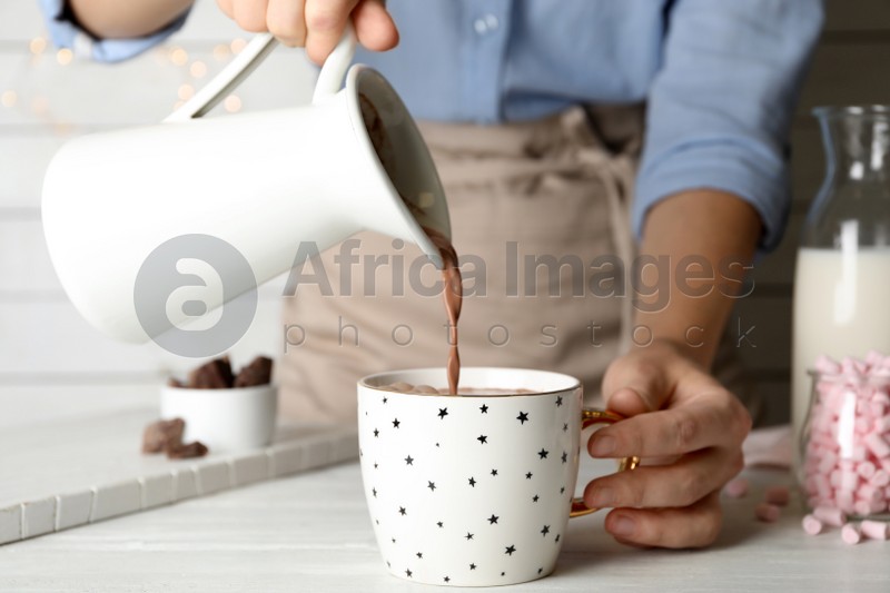 Woman pouring hot cocoa drink into cup on white wooden table, closeup