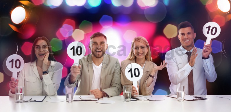 Panel of judges holding signs with highest score at table against blurred background. Bokeh effect
