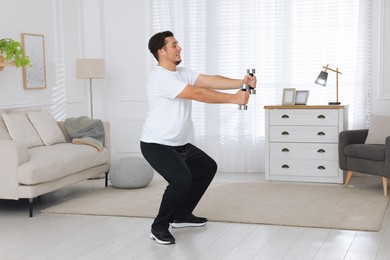 Overweight man doing squat exercise with dumbbells at home