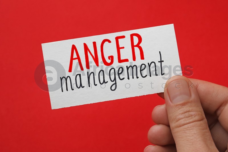 Photo of Man holding card with words Anger Management on red background, closeup