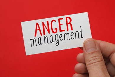 Man holding card with words Anger Management on red background, closeup
