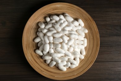 White silk cocoons with plate on wooden table, top view