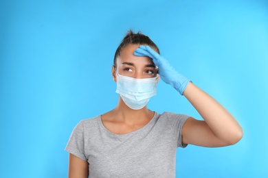 Stressed woman in protective mask on light blue background. Mental health problems during COVID-19 pandemic