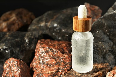 Bottle of face serum on wet stones, closeup