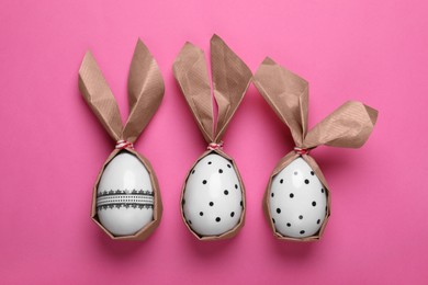 Photo of Easter bunnies made of craft paper and eggs on pink background, flat lay
