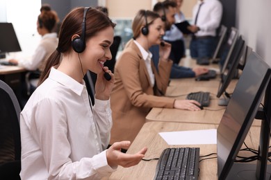 Photo of Call center operators working in modern office, focus on young woman with headset