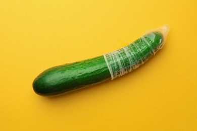 Cucumber with condom on orange background. Safe sex