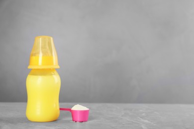 Feeding bottle with infant formula and scoop of powder on grey table, space for text. Baby milk