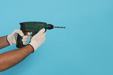 Worker in gloves with power drill on light blue background, closeup. Space for text