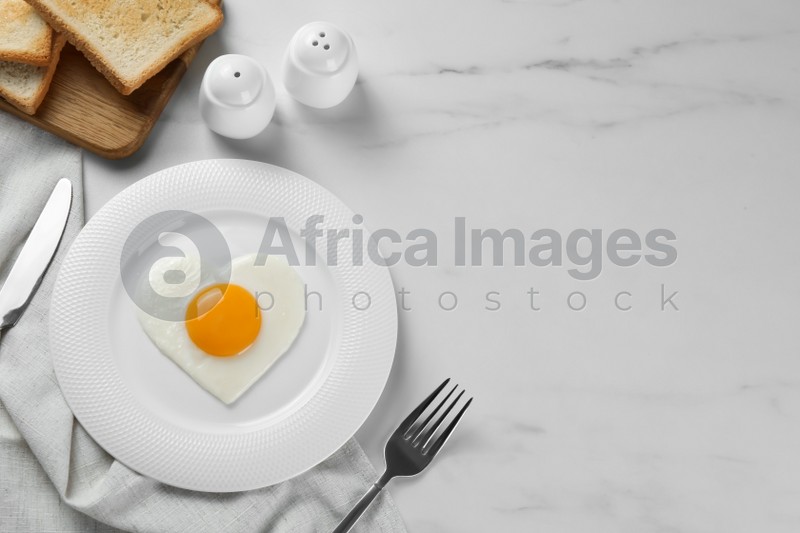 Romantic breakfast with heart shaped fried egg served on white marble table, flat lay. Space for text