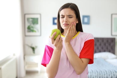 Young woman with sensitive teeth and apple at home