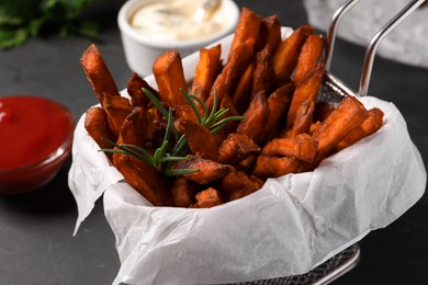 Frying basket with sweet potato fries and sauces on black table, closeup