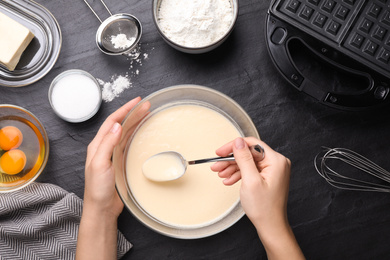 Photo of Woman preparing dough for Belgian waffles at black table, top view