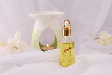 Aroma lamp and freesia essential oil on white cloth, space for text